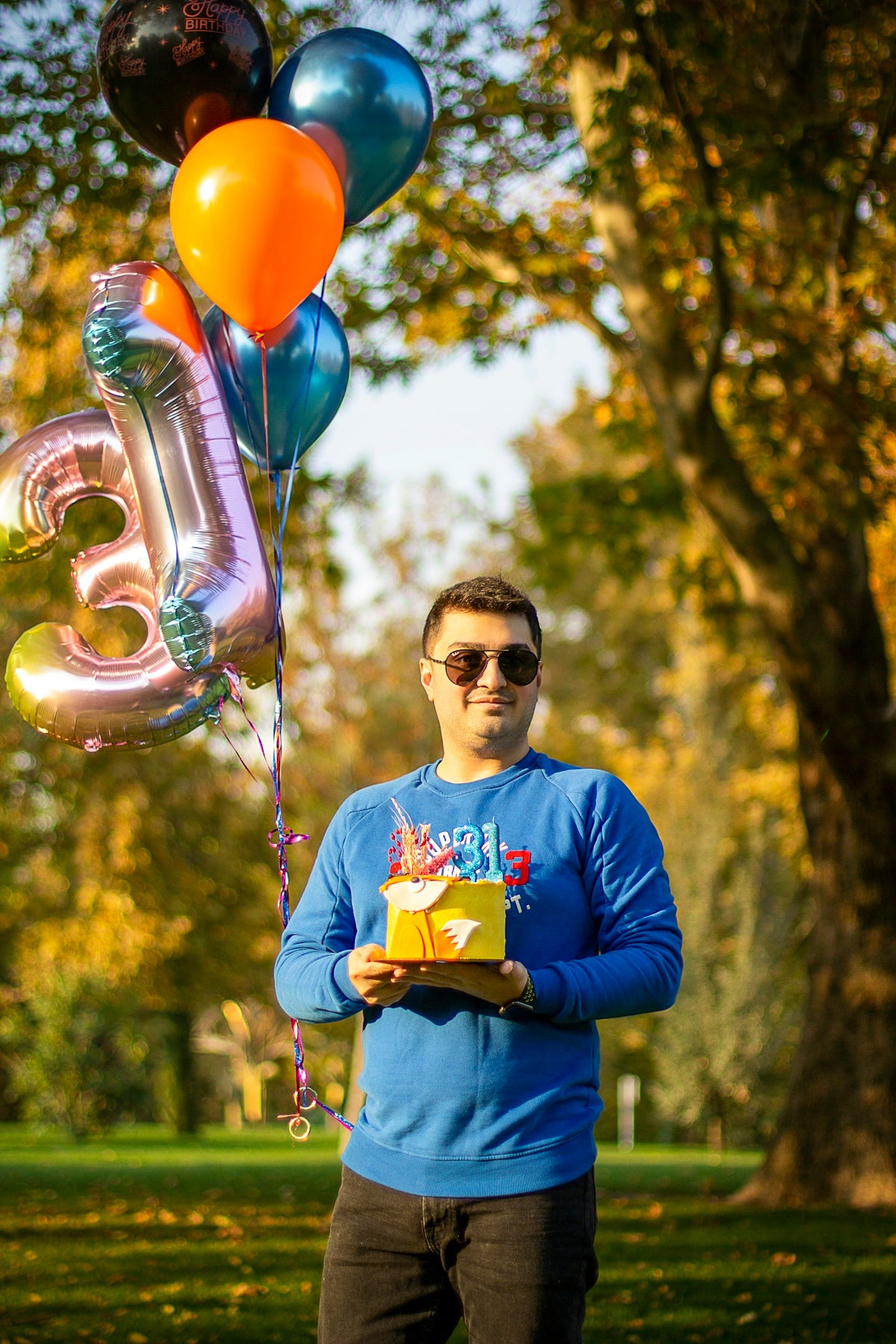 a man holding a birthday cake and balloons
