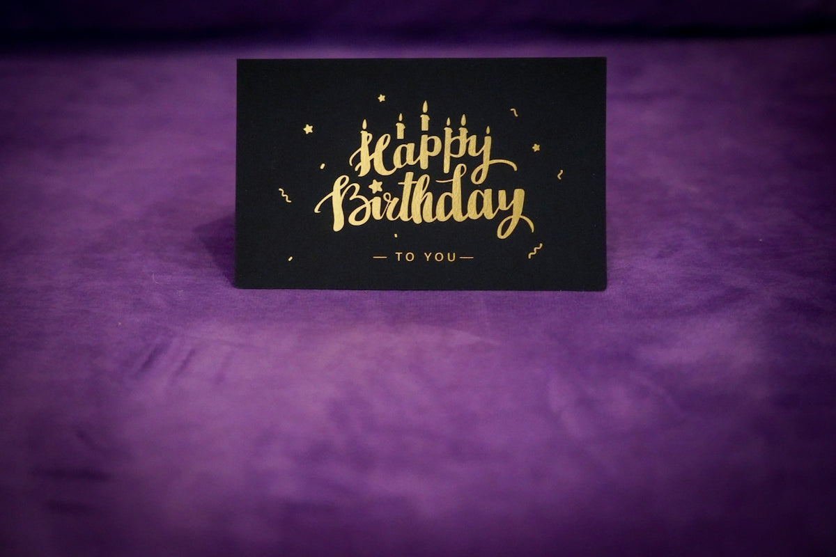 A black and gold happy birthday card on a purple background