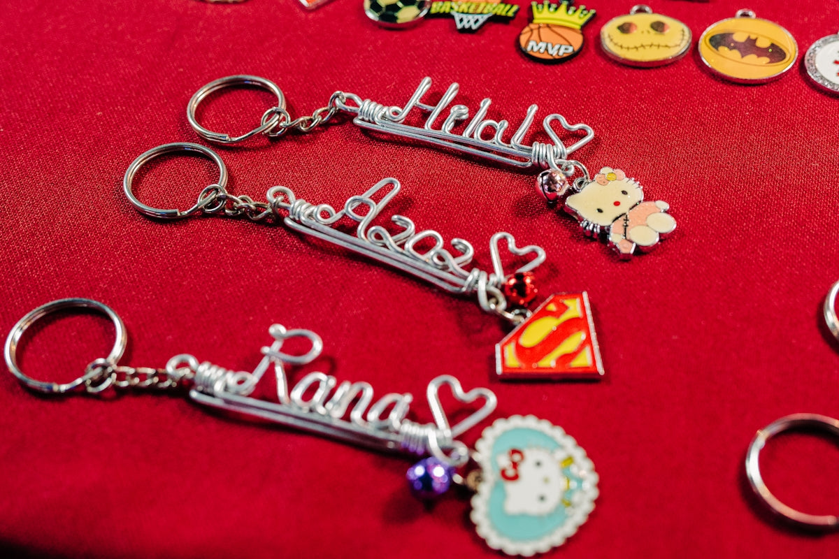 Three personalized name keychains with charms on a red surface.
