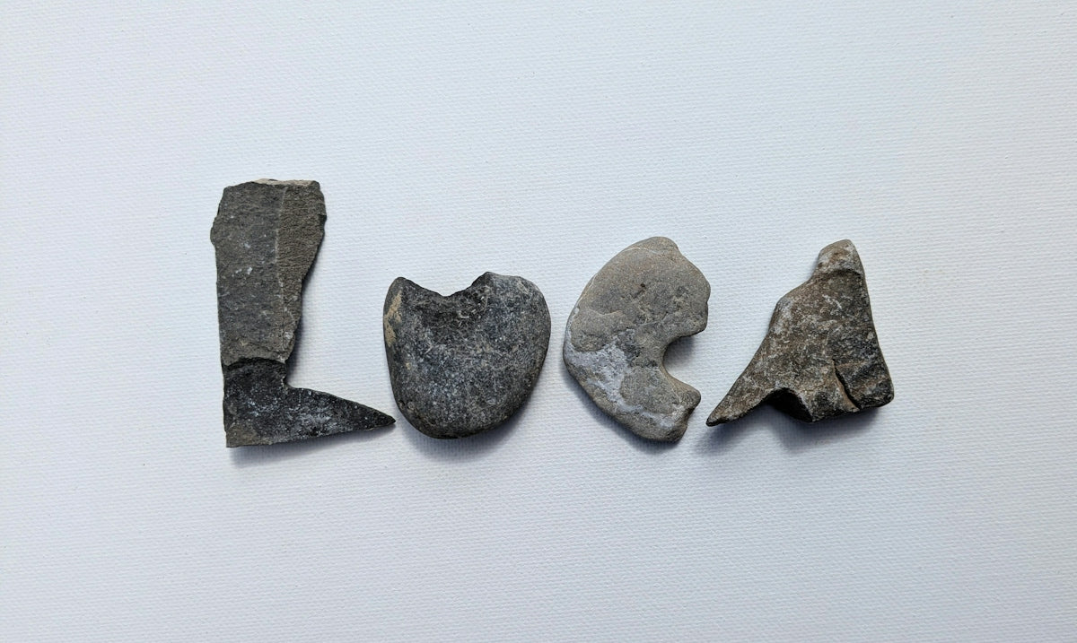 Grey stones spell 'loca' on a white background.